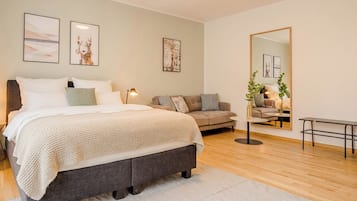 Un dormitorio moderno con una cama grande, un sofá, una mesita y un espejo.