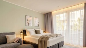 A modern bedroom with a bed, a sofa, a round ottoman, and a large window with curtains. - Limehome Dresden Wallstraße (Dresden)