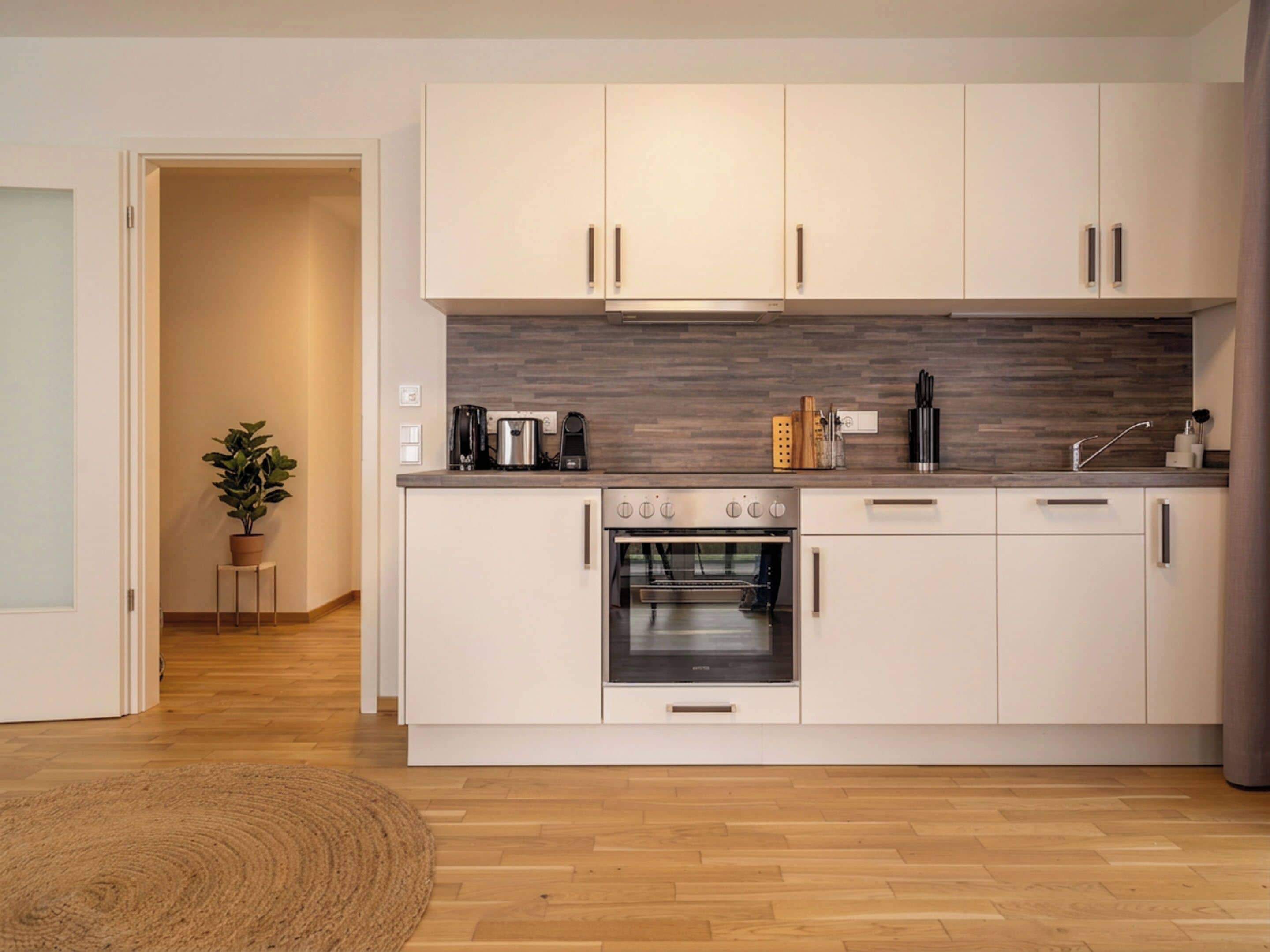 Een moderne keuken met witte kastjes, een inbouwoven en een houten spatwand.