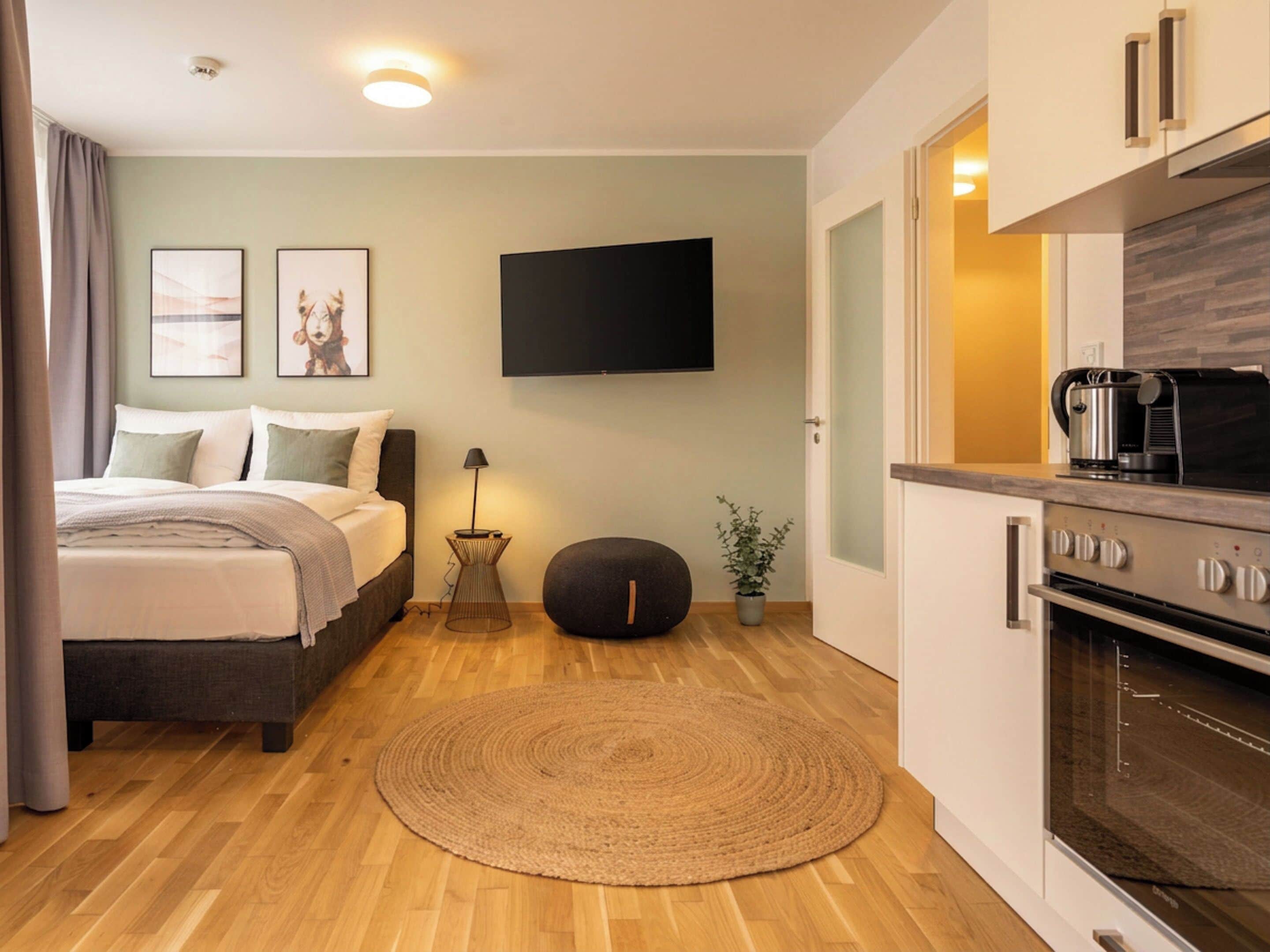 Une chambre d’hôtel moderne équipée d’un lit, d’un téléviseur à écran plat, d’une kitchenette et d’un plancher en bois.