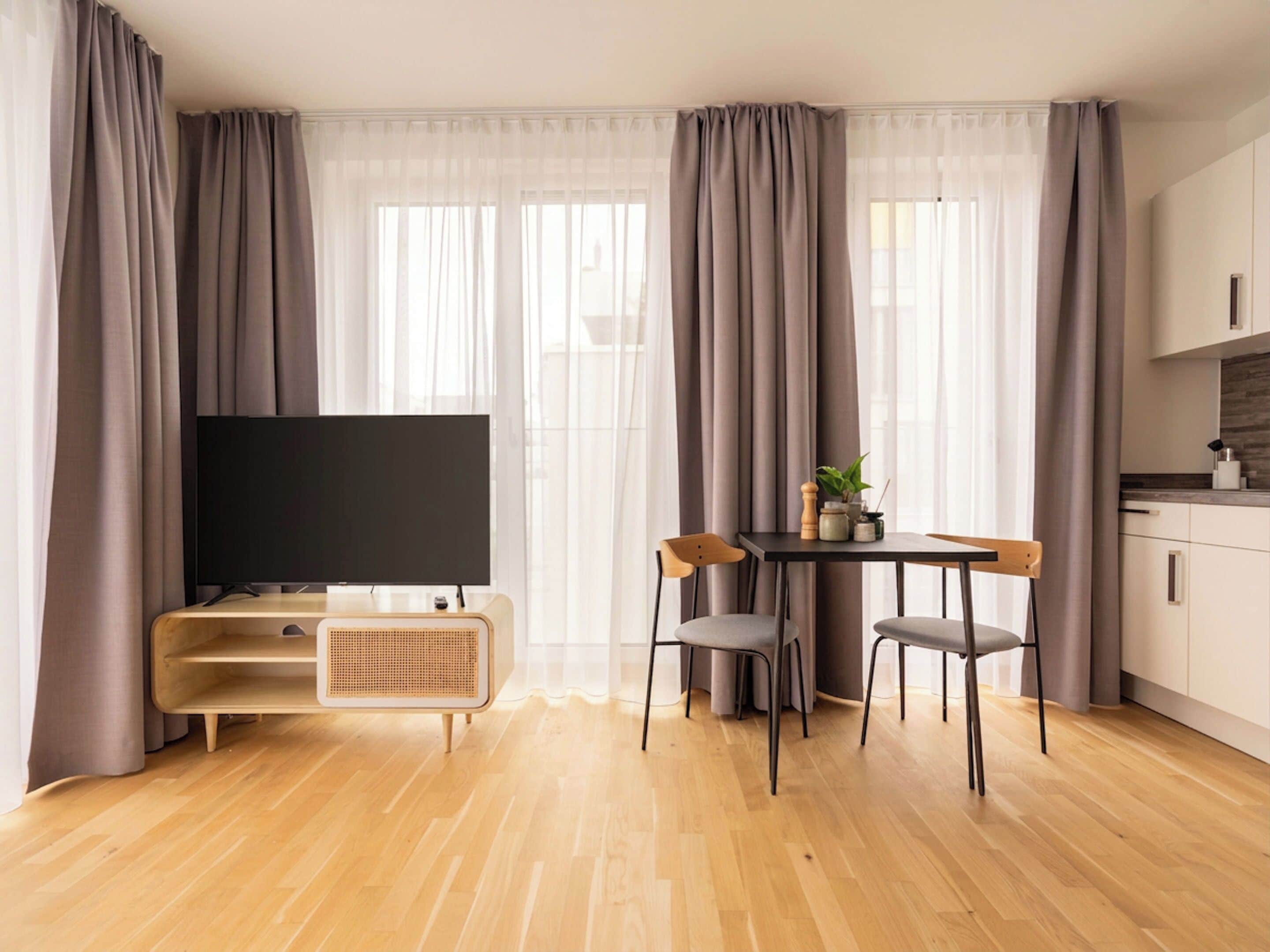 A modern living room with a flat-screen TV, wooden furniture, and a kitchen area.