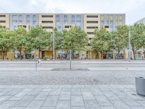En modern byggnad med flera våningar, stora fönster och en stenlagd yta med träd framför.