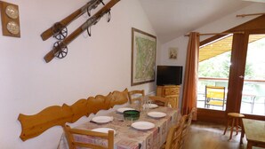 Un coin repas avec une table en bois dressée pour quatre personnes, des chaises, un téléviseur et une carte accrochée au mur.