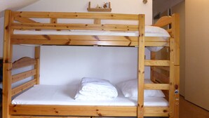 Un lit superposé à deux niveaux, avec une literie blanche et une petite étagère au-dessus du lit supérieur.