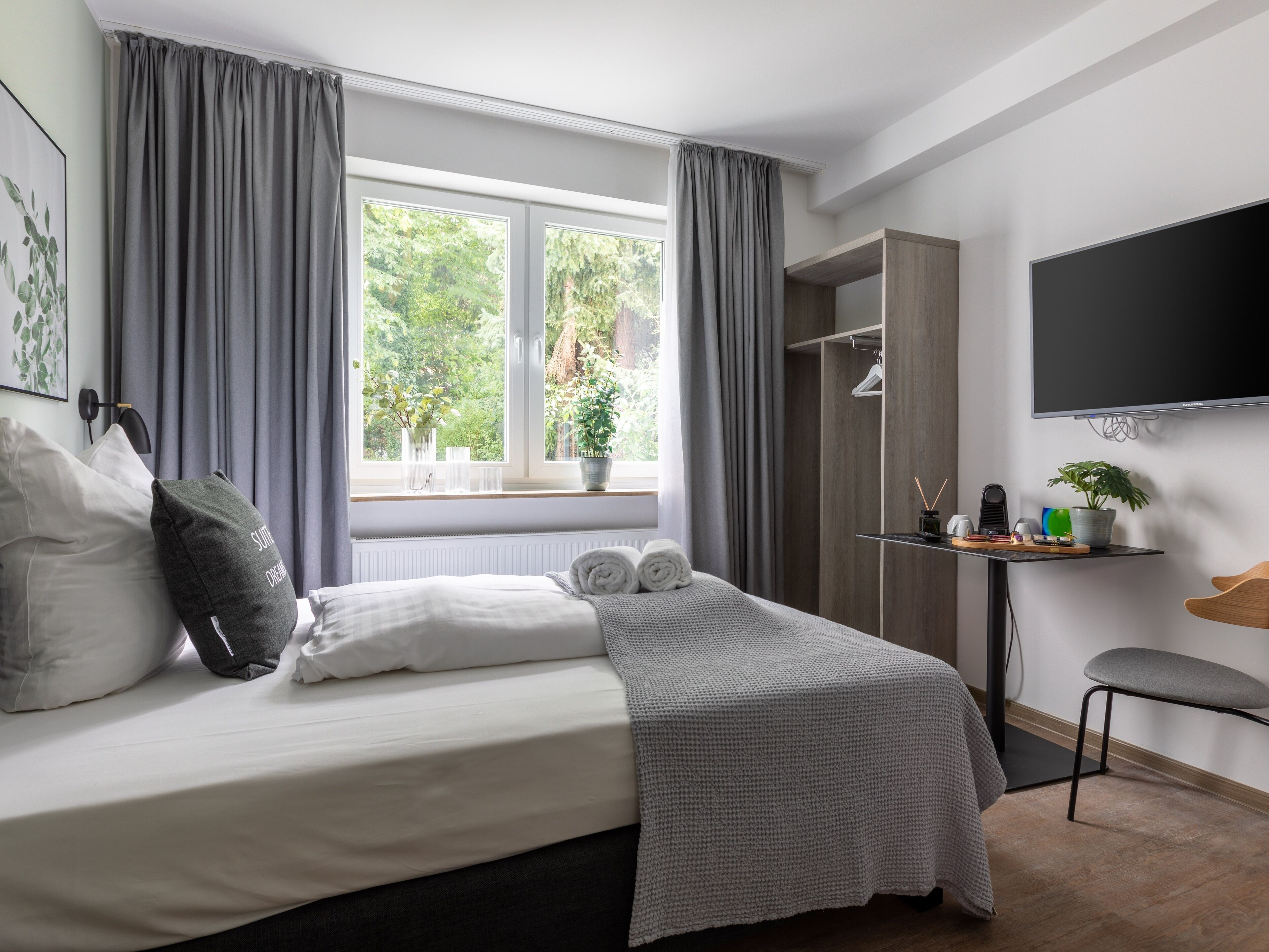 A modern bedroom with a bed, a desk, a chair, a TV, and a window with curtains.