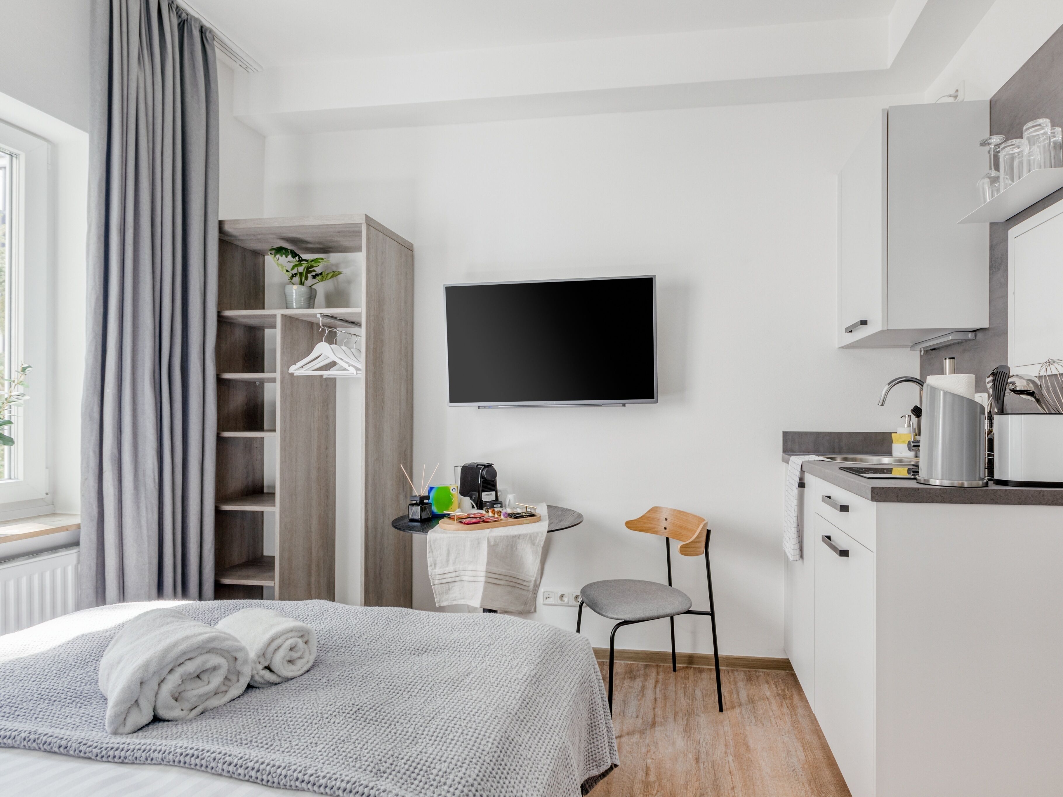 Una camera d'albergo moderna con un letto, una scrivania, una sedia, una TV e angolo cottura.