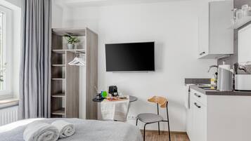 Una camera d'albergo moderna con un letto, una scrivania, una sedia, una TV e angolo cottura.