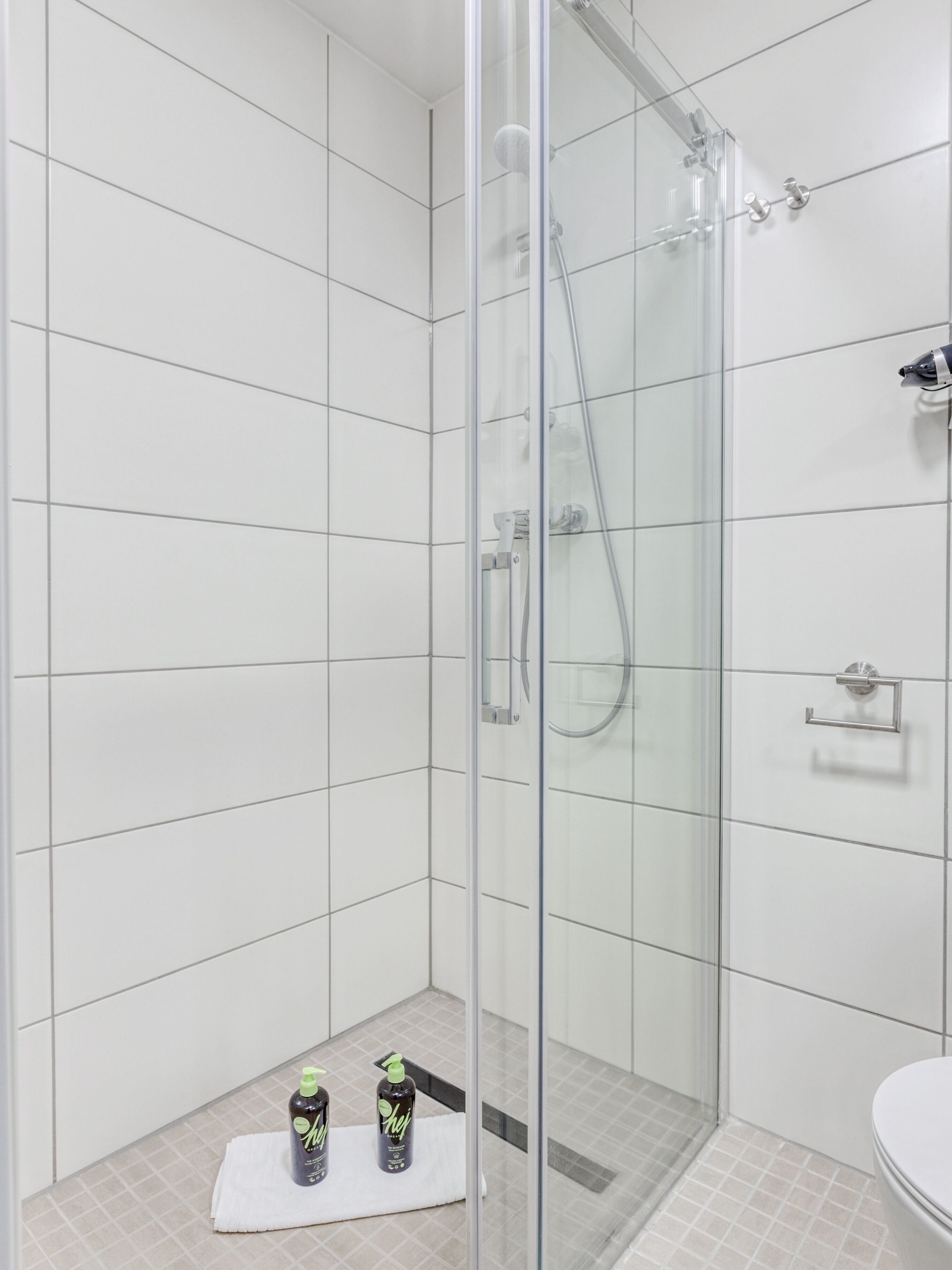 A modern bathroom with a glass-enclosed shower, white tiled walls, and a white sink.