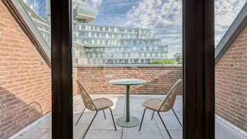 A balcony with a round table and two wicker chairs, overlooking a modern building with glass windows.