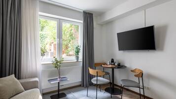 Ein modernes Zimmer mit einer Couch, einem kleinen Tisch mit Stühlen, einer Topfpflanze und einem Fernseher an der Wand.