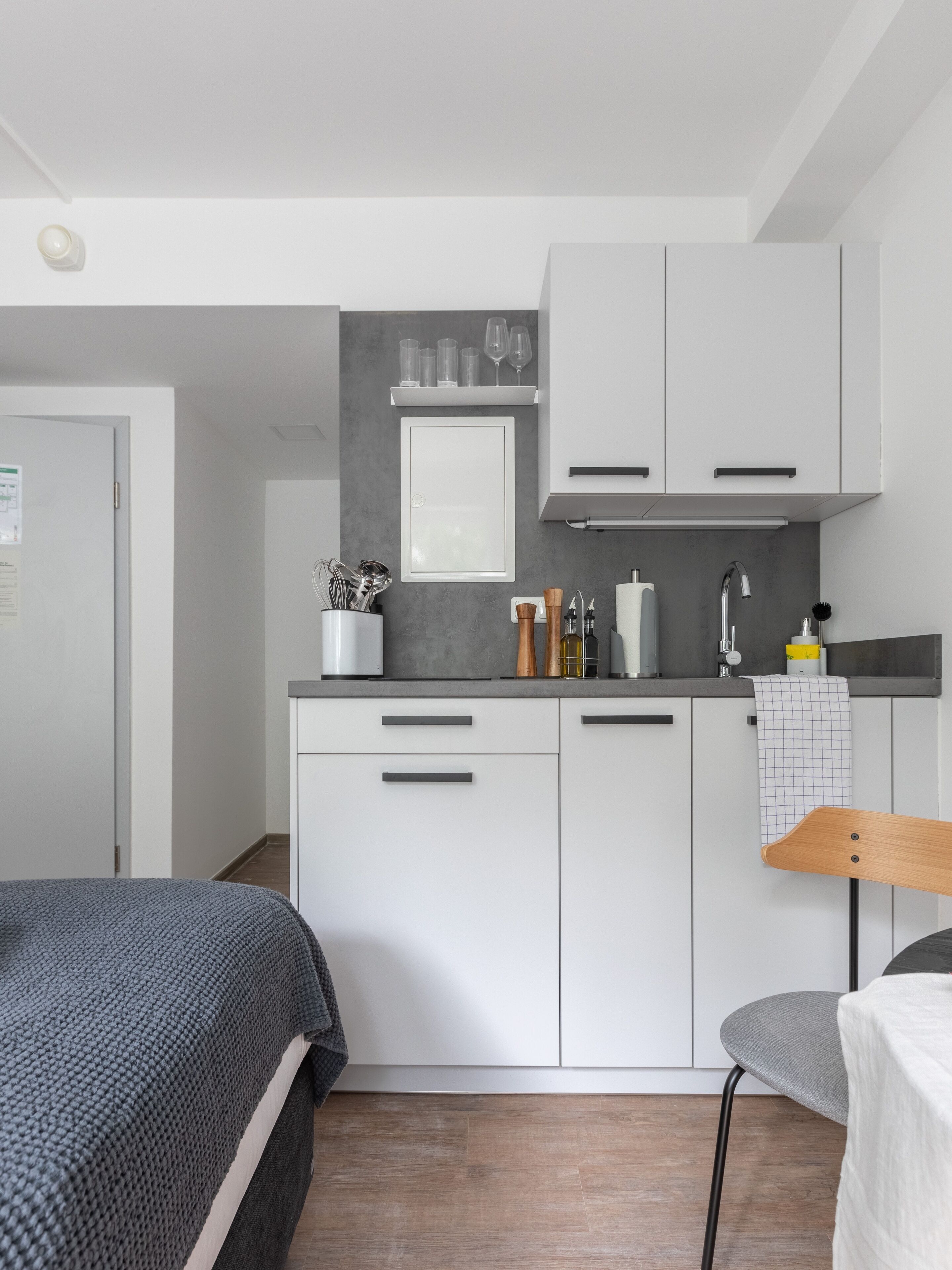 A modern kitchen with white cabinets, a grey countertop, and a small shelf with glasses.