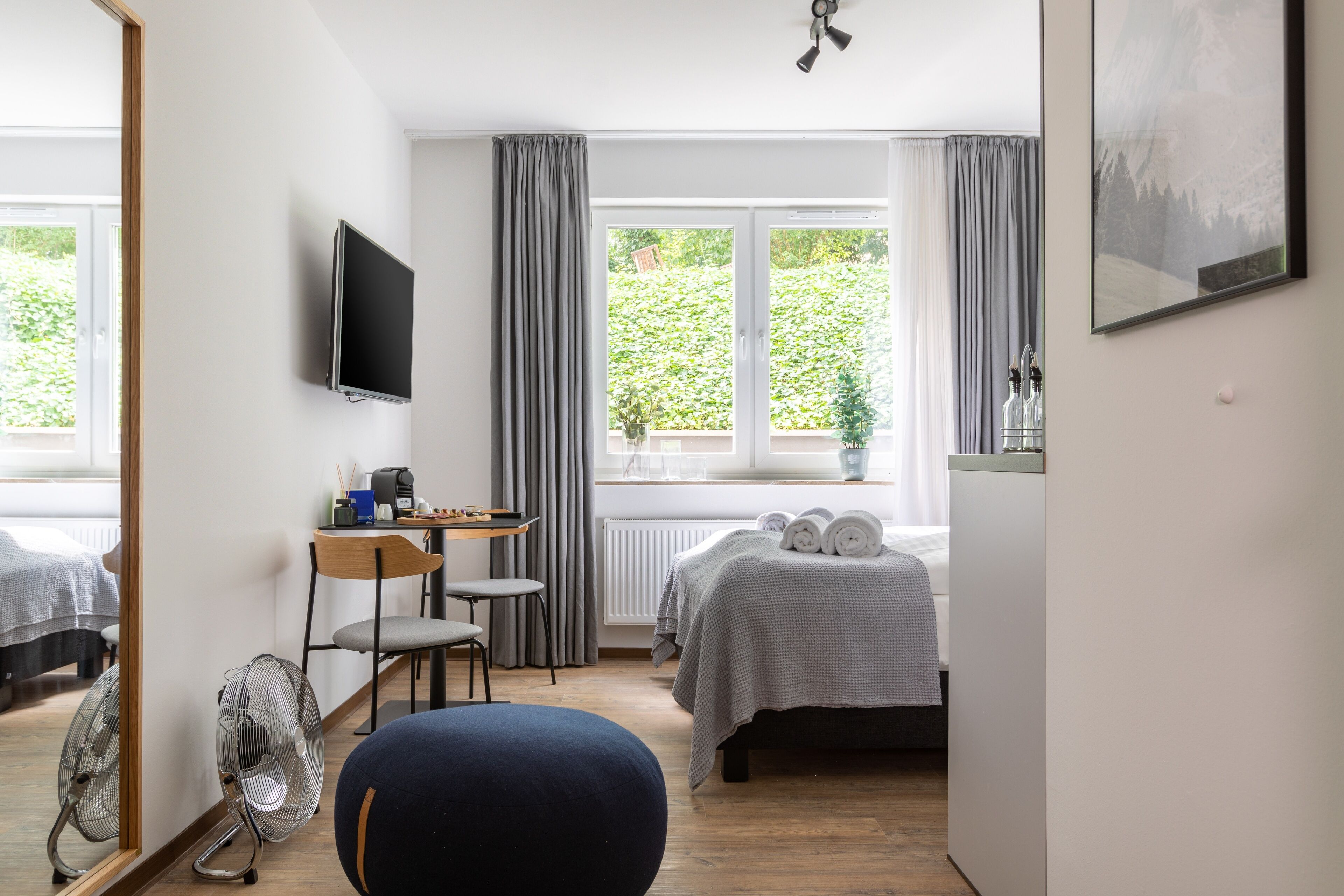 A hotel room with a bed, a desk with a chair, a TV, and a window with curtains.