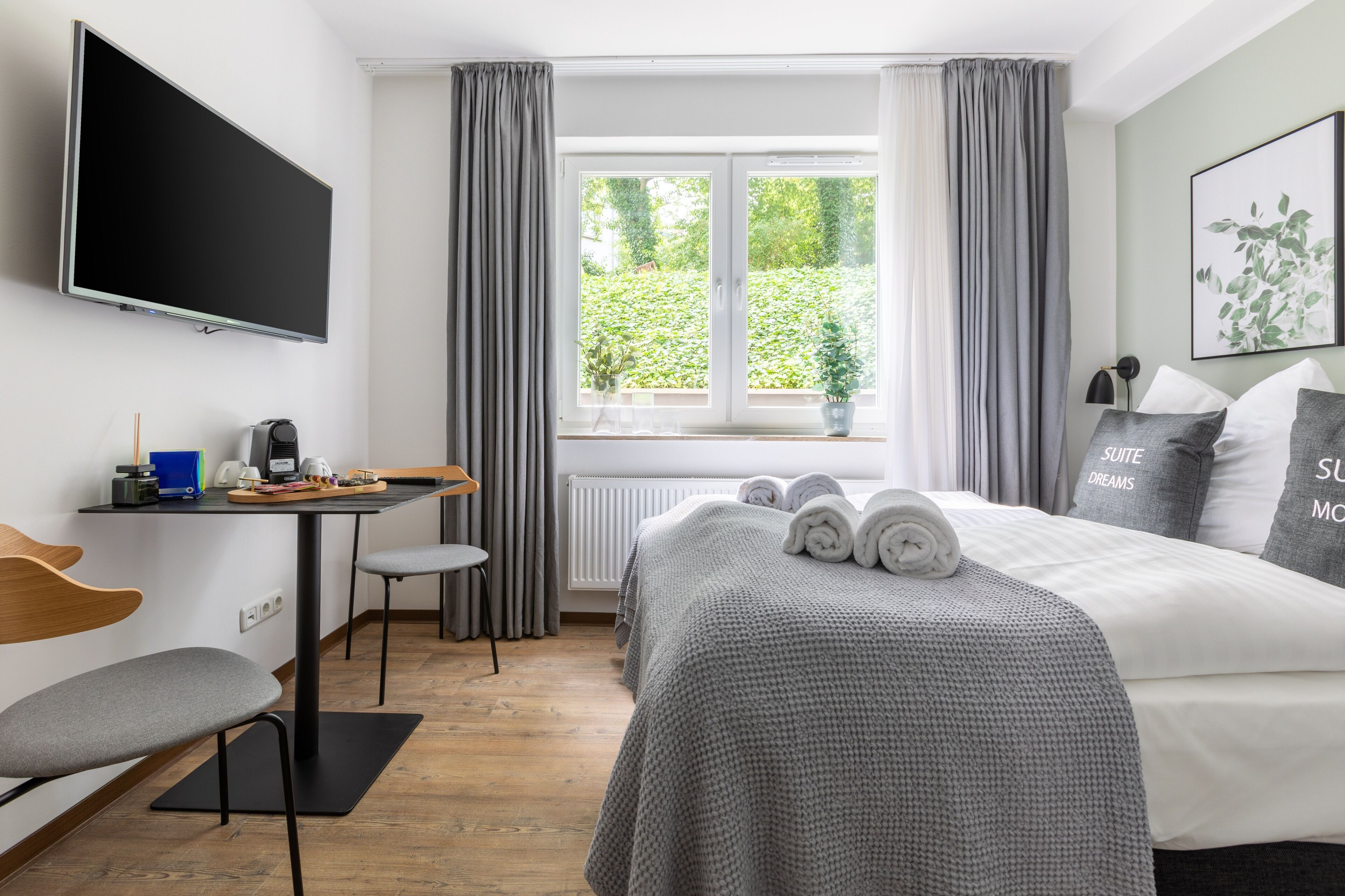 A hotel room with a bed, a desk, a chair, a TV, and a window with curtains.