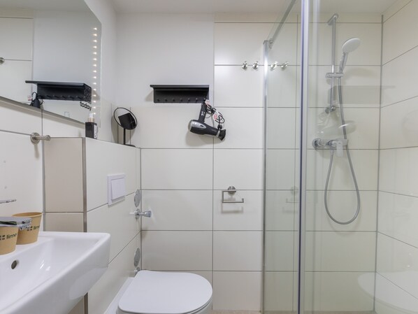 A modern bathroom with a glass-enclosed shower, a white sink, and a toilet. - Limehome Hannover Bleichenstraße (Hannover)