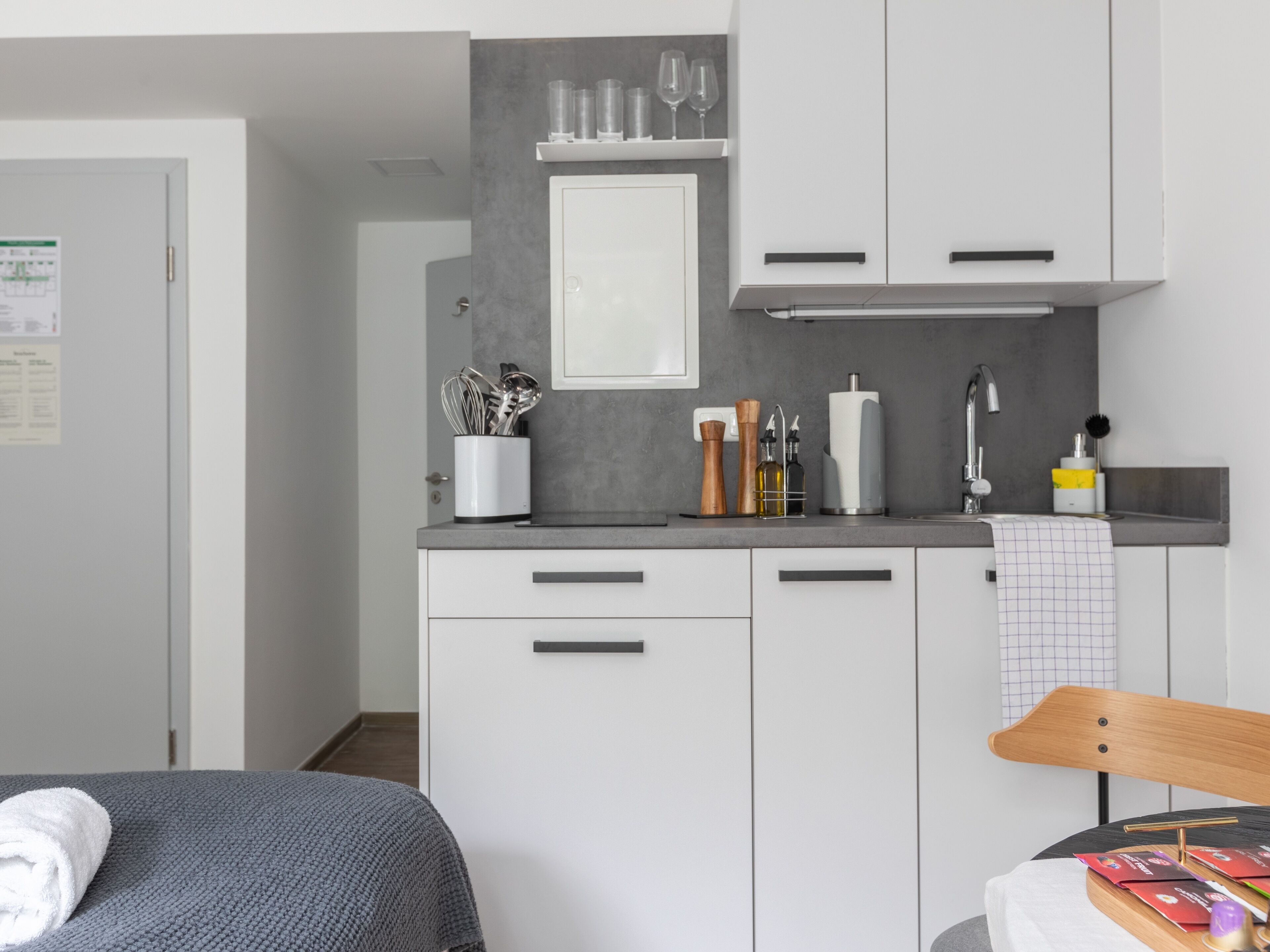 A compact kitchen with white cabinets, a countertop, and a sink. There are utensils and a bottle on the counter.