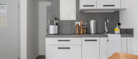 A compact kitchen with white cabinets, a countertop, and a sink. There are utensils and a bottle on the counter.