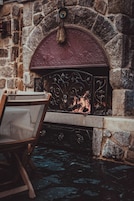 Una chimenea de piedra con una rejilla metálica decorativa, una silla de madera al frente y una pared de piedra.