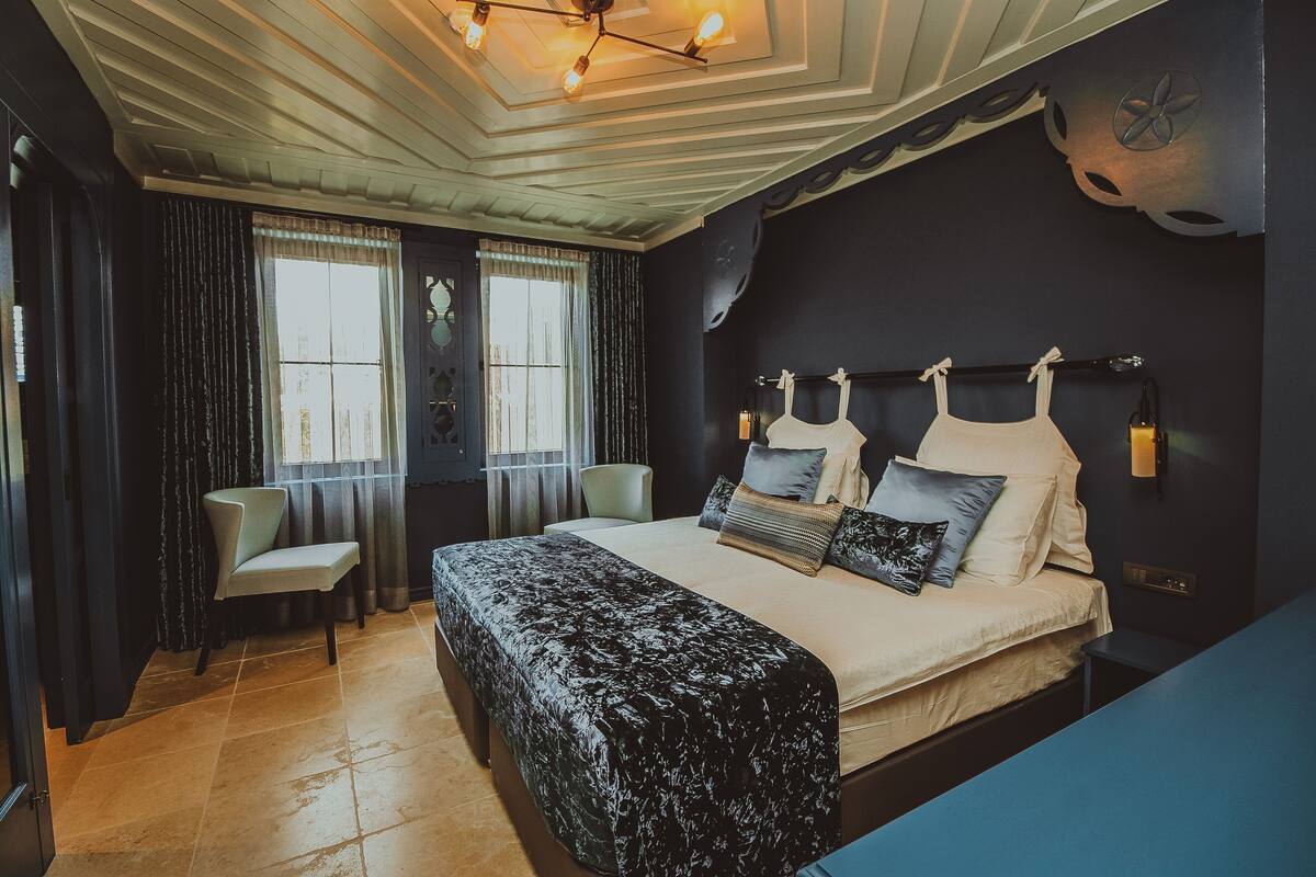 A bedroom with a large bed, a chair, a desk, and a window.