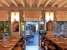 Un restaurante con mesas de madera dispuestas para comer, ventanas amplias y plantas en macetas.
