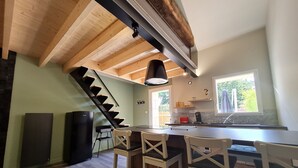 Una cocina moderna con techo de madera, escalera negra y comedor con sillas blancas.