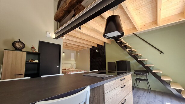 Una cocina moderna con una isla central, techo de madera y una escalera.