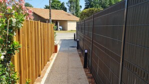 Un sendero estrecho que conduce a una casa con tejado de tejas, delimitado por una valla de madera a un lado y una valla de metal al otro.