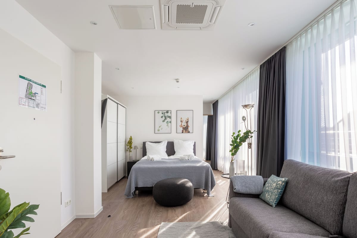 A modern bedroom with a bed, a sofa, a floor lamp, and a large window with curtains.