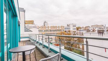 Un balcón con una mesa y sillas, con vista a un paisaje urbano con edificios y árboles.