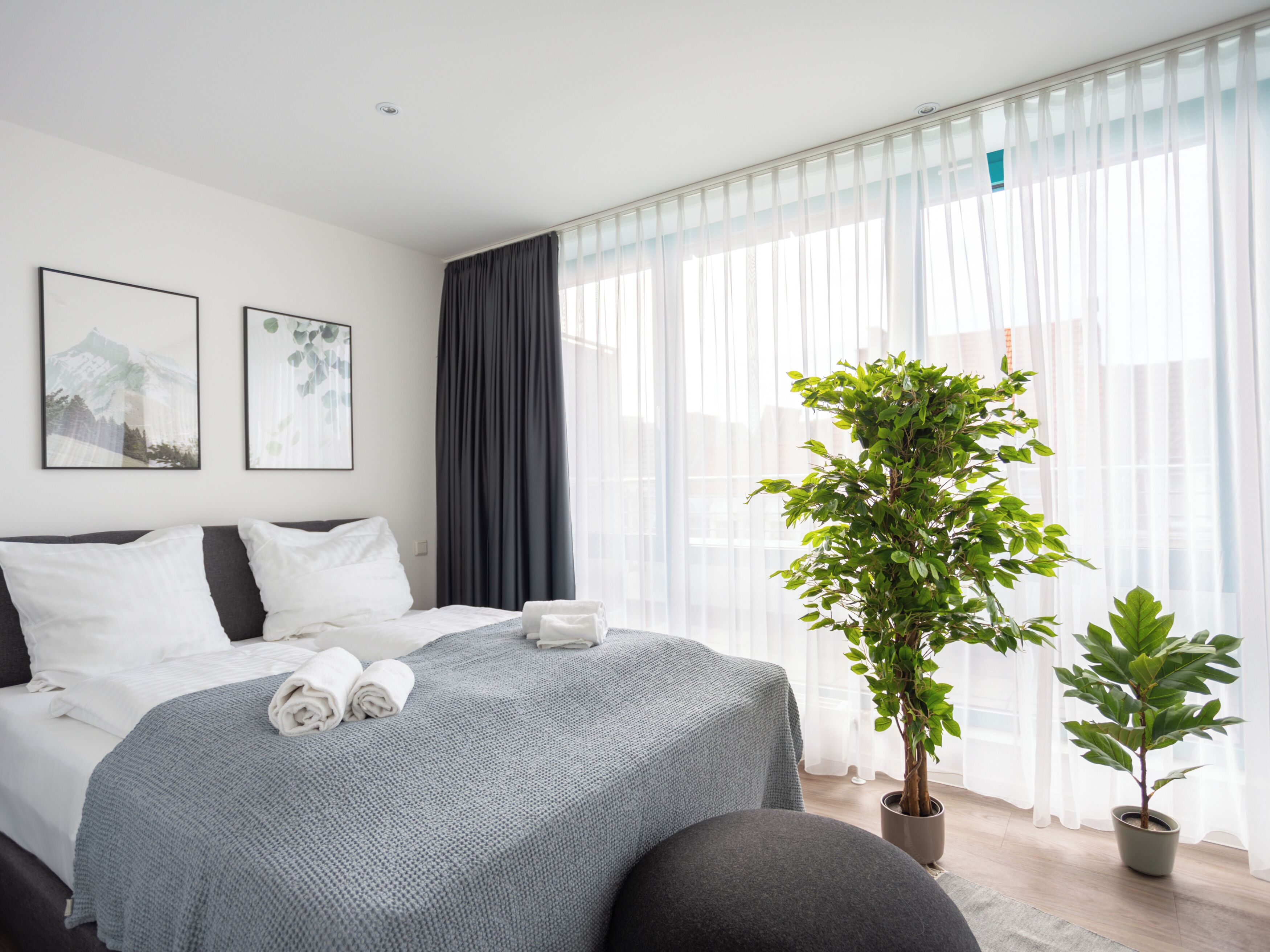 Une chambre d’hôtel moderne avec un grand lit, une plante en pot et des œuvres d’art accrochées au mur.