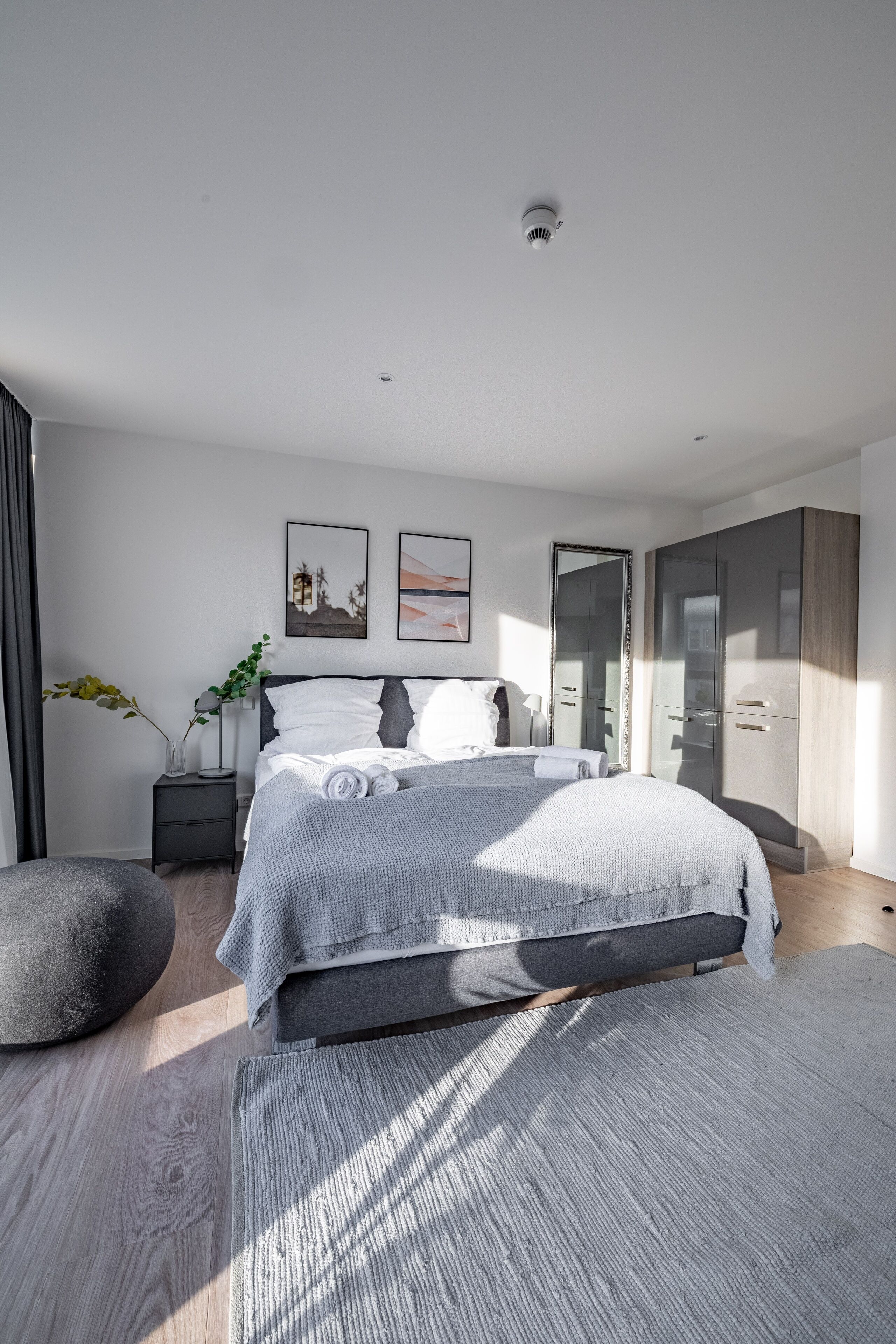 Een moderne slaapkamer met een groot bed, een nachtkastje, een kledingkast en een spiegel.