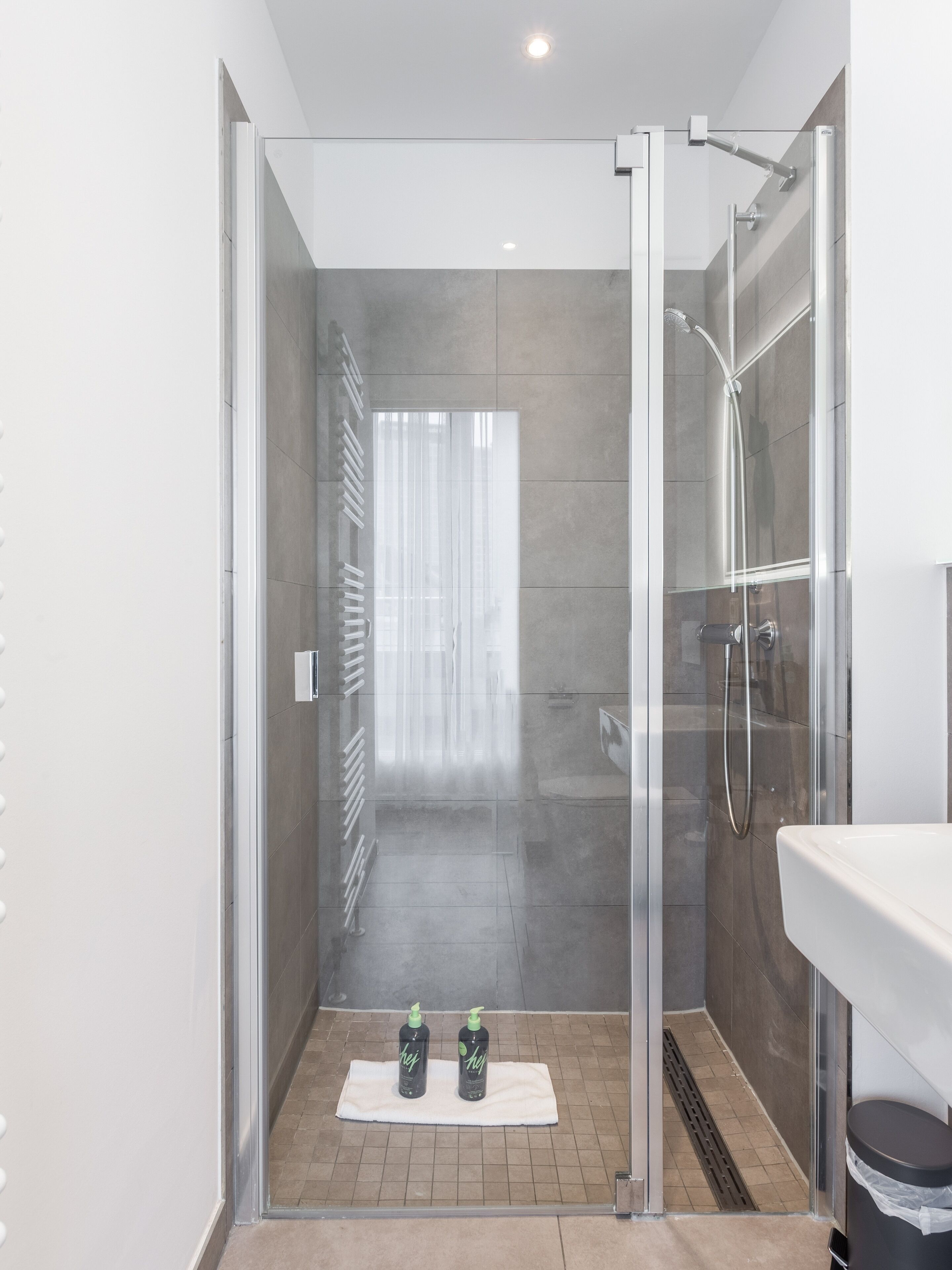 A modern shower with a glass door, a white sink, and a towel on the floor.