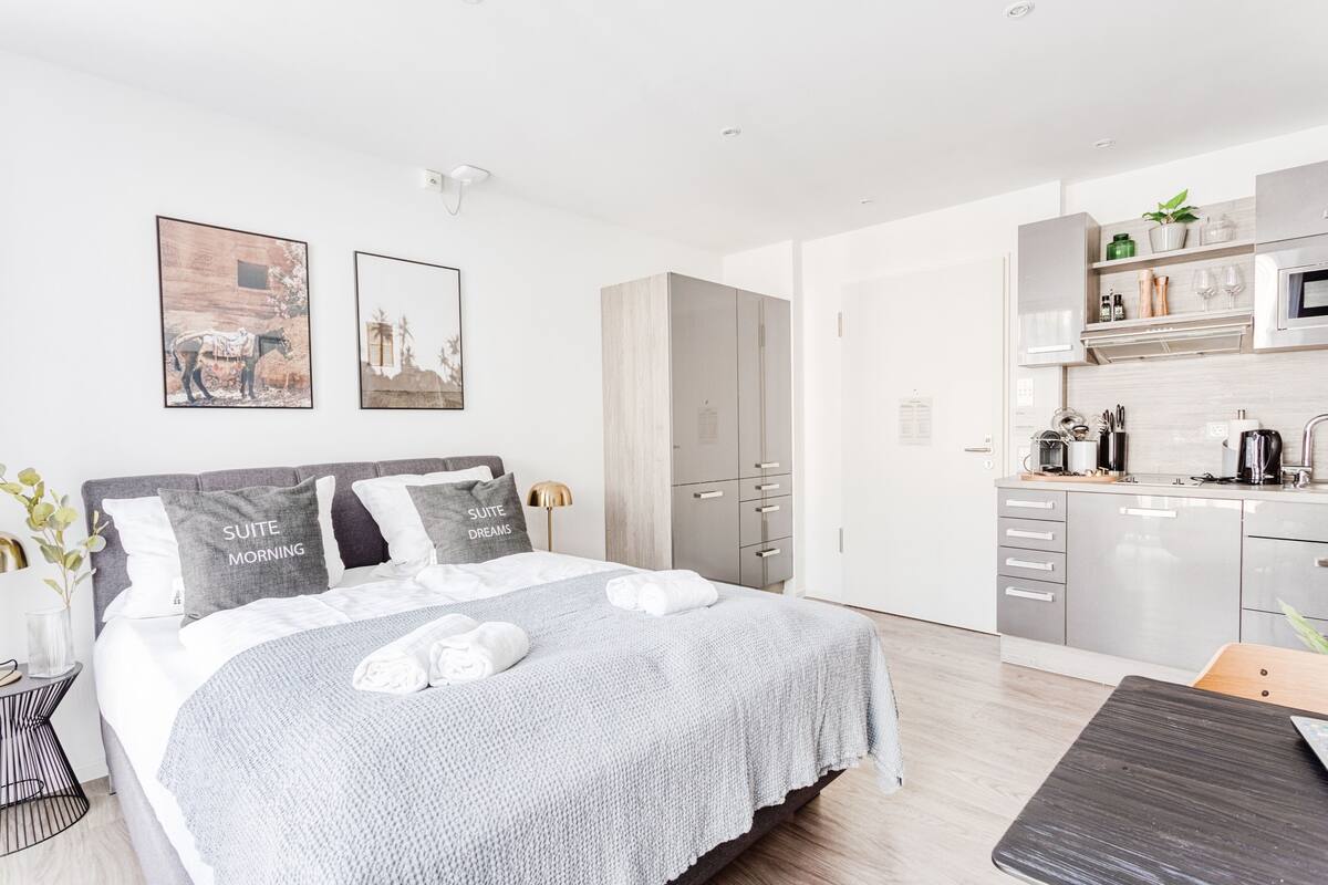 A modern hotel room with a large bed, a separate kitchenette, and artwork on the walls.