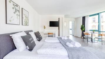 A modern hotel room with a large bed, a desk, and a balcony with a view.