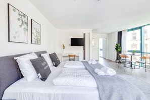 A modern hotel room with a large bed, a desk, and a balcony with a view.