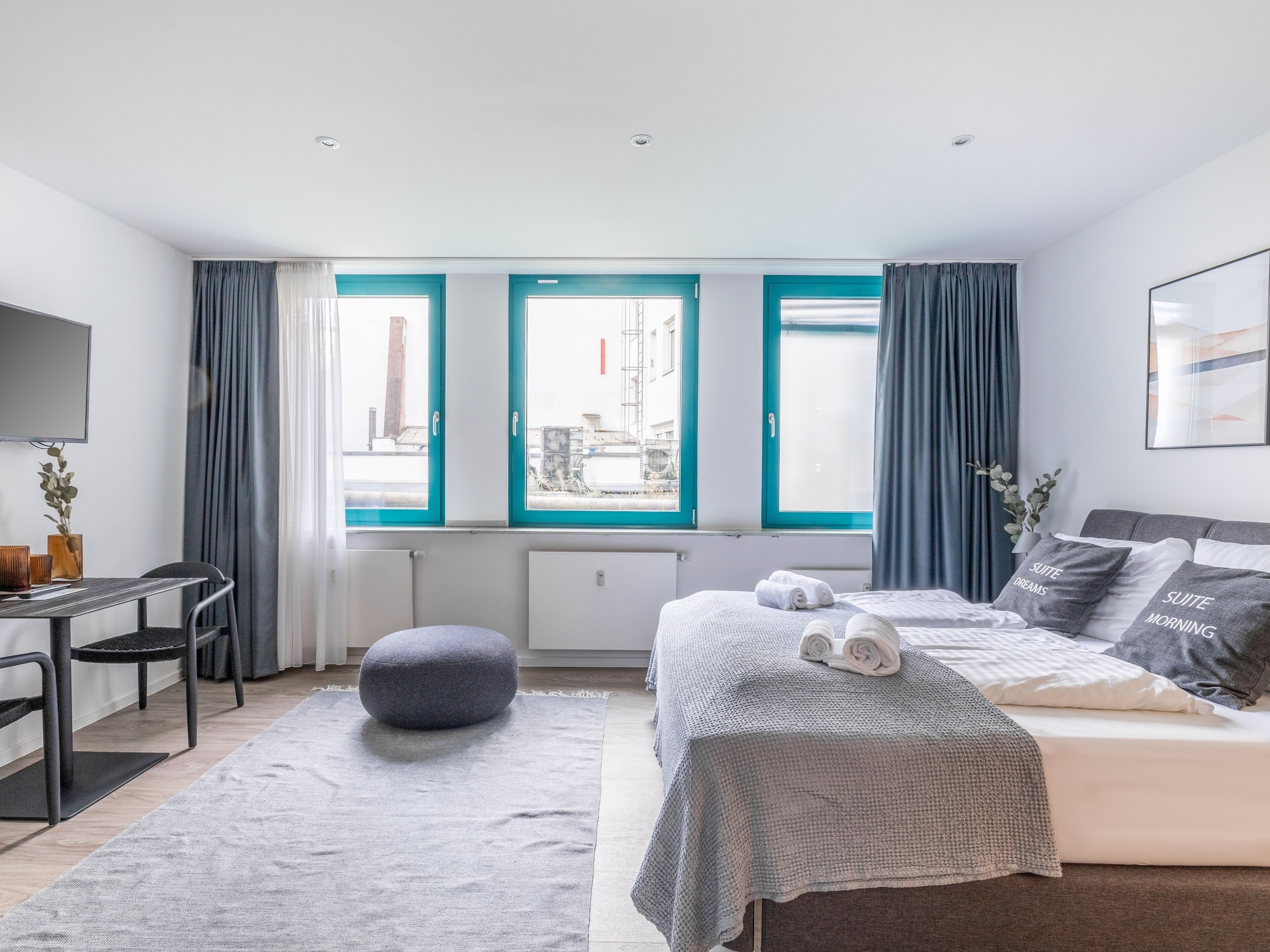 A modern bedroom with a bed, a desk, and a view through large windows.