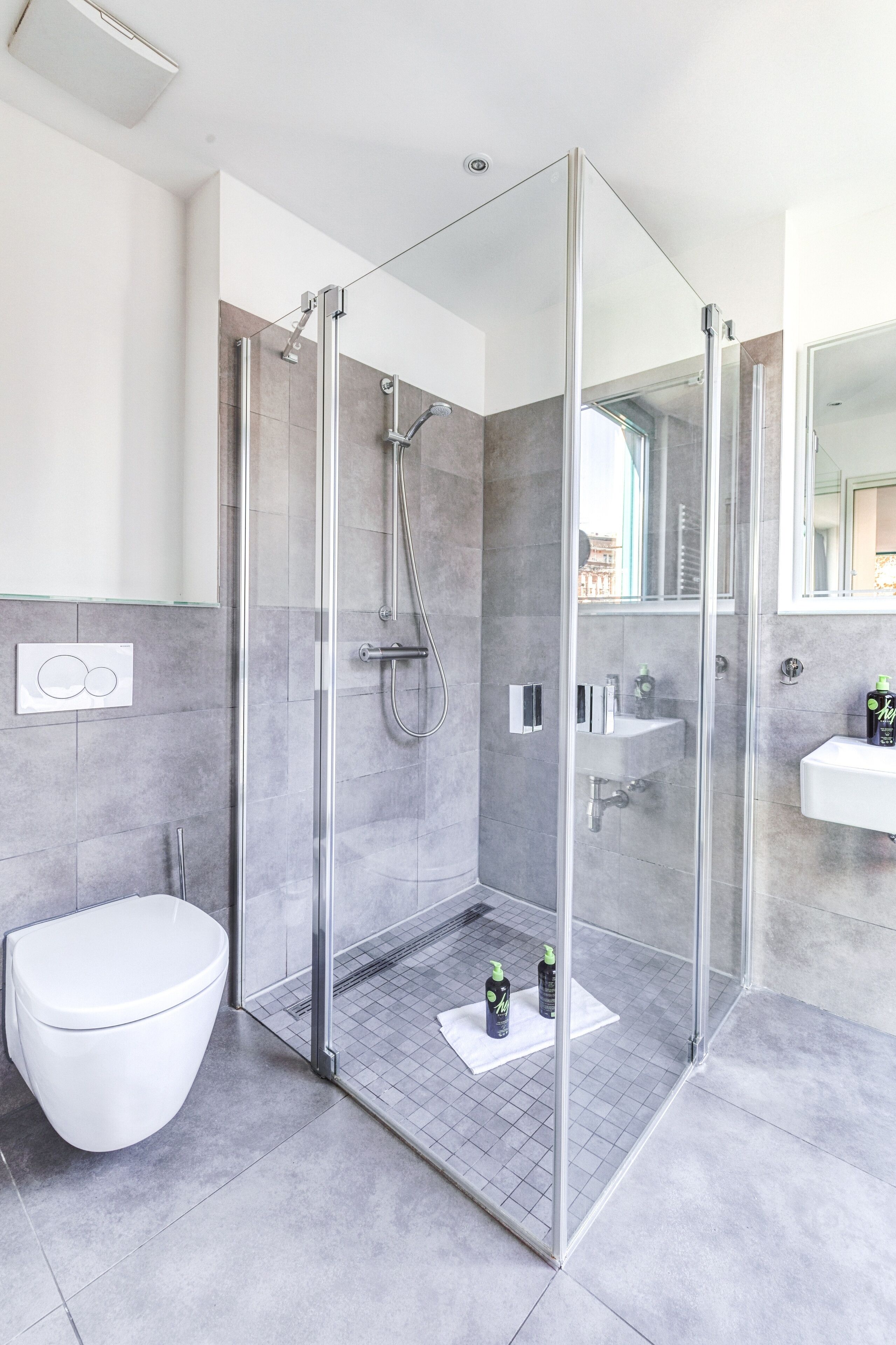 A modern bathroom with a glass-enclosed shower, a white toilet, and a sink with a mirror above it.