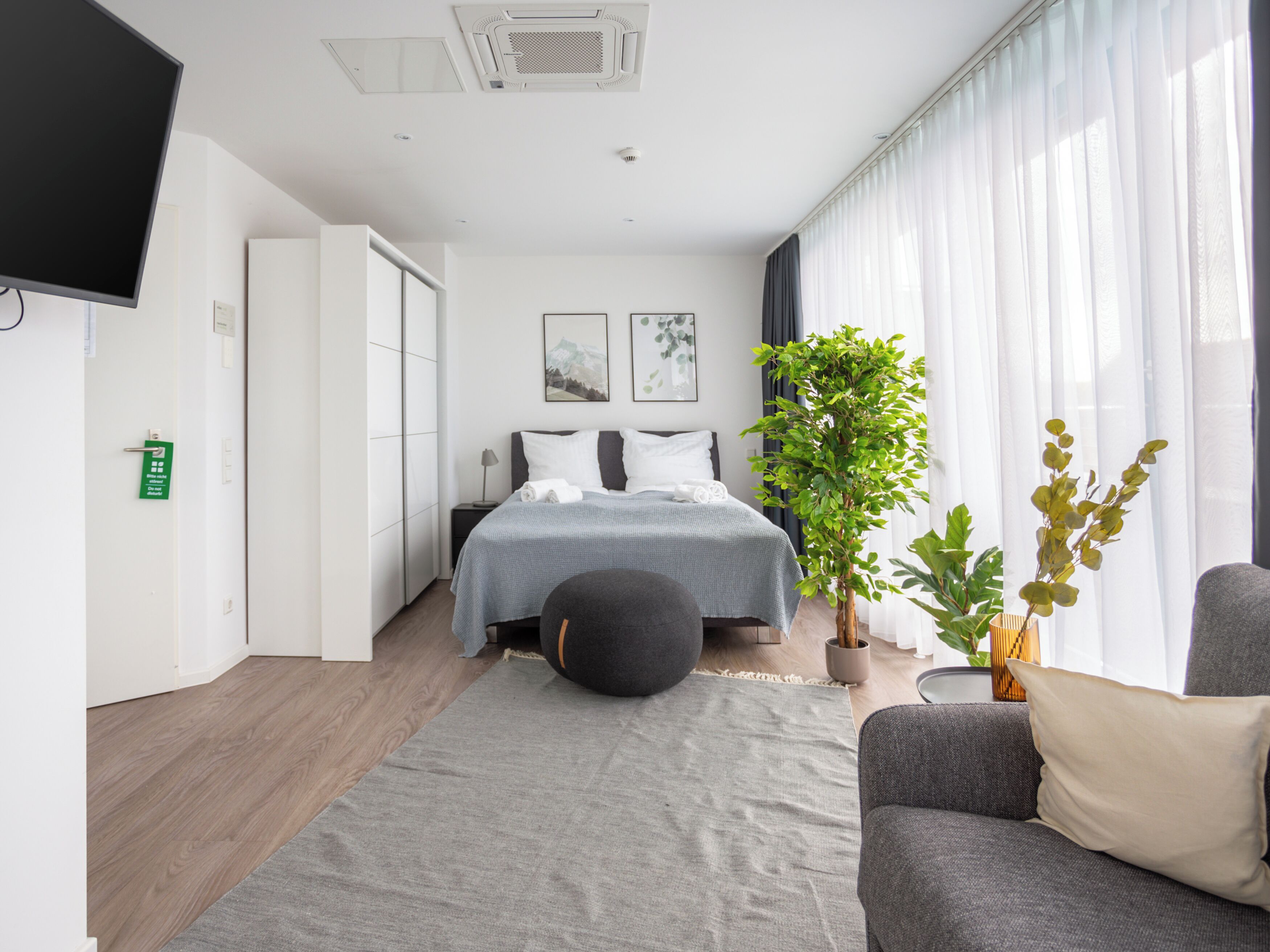 Ein modernes Hotelzimmer mit Bett, einer Couch, einer Topfpflanze und einem Fernseher.