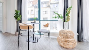 Una habitación moderna con un ventanal grande, una mesa de comedor con sillas, una silla de mimbre y una planta en maceta.