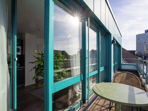 Un bâtiment moderne doté de grandes fenêtres, d’un balcon avec une table et d’une plante en pot.