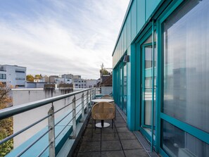 A balcony with a table and chairs, overlooking a river with buildings in the background.