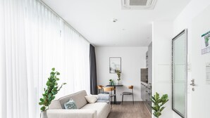 Una sala moderna con sofá, una mesa de comedor y sillas. Cuenta con una zona de cocina con armarios y un refrigerador.