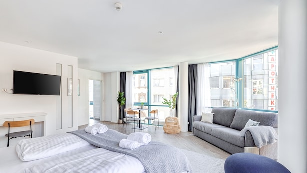 Una habitación de hotel moderna con una cama grande, un sofá, un televisor y un área de comedor con una mesa y sillas.