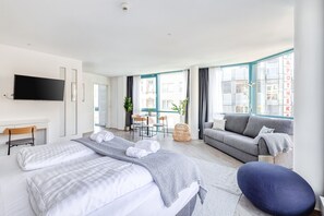 A modern hotel room with a large bed, a sofa, a TV, and a dining area with a table and chairs. - Limehome Köln Friesenplatz (Cologne)