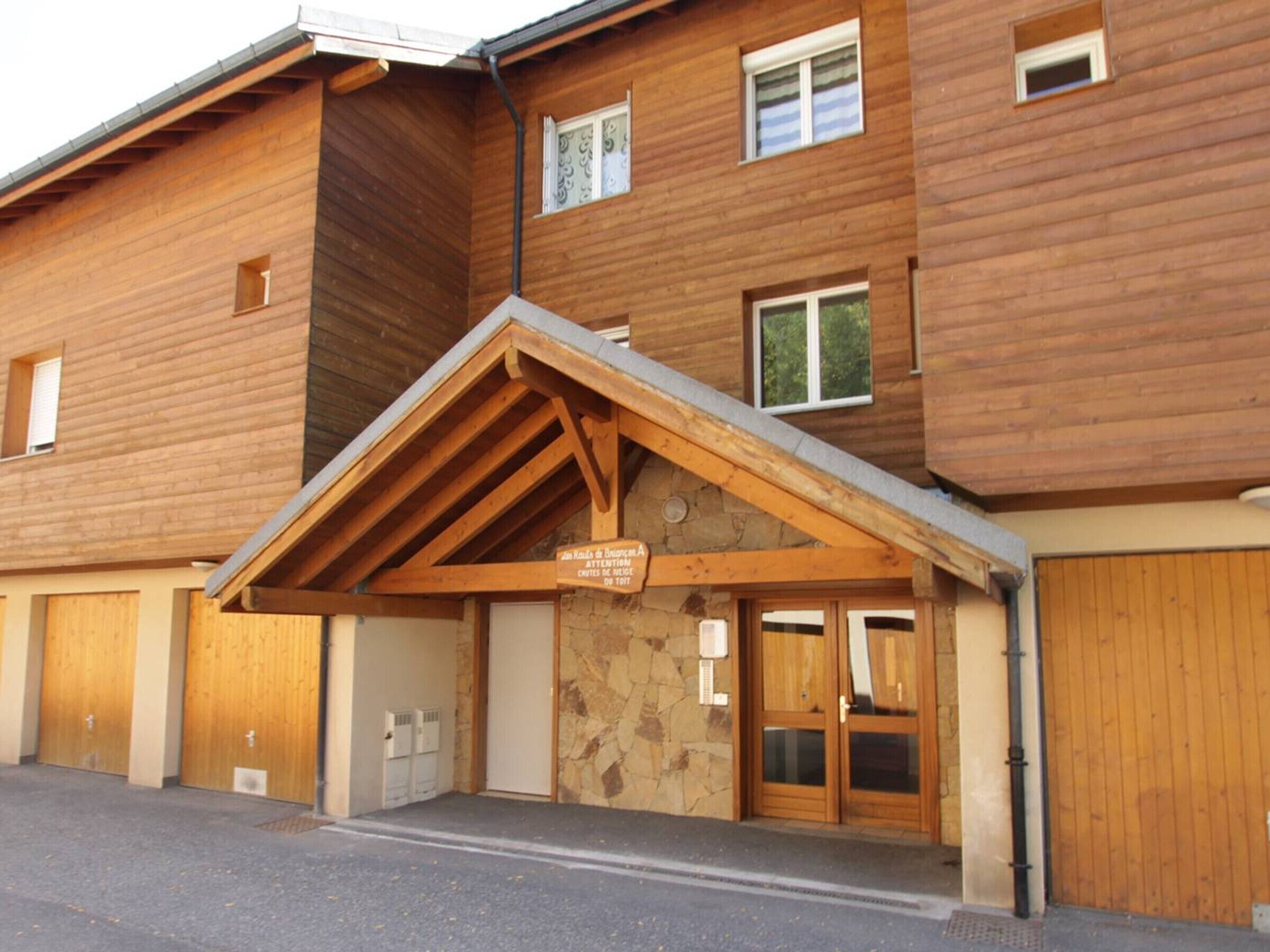 A wooden building with a covered entrance, stone walls, and a sign indicating a ski slope.