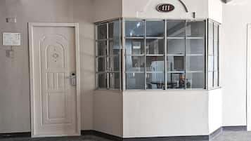A corner room with a white door, a window with multiple panes, and a number sign above the window.