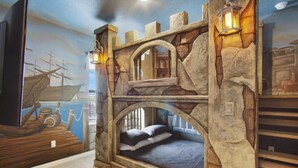 A room with a stone wall, a bed, and a mural of a ship.