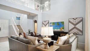Ein geräumiges Wohnzimmer mit hoher Decke, einer Treppe, einem großen Gemälde und einem modernen Kamin.
