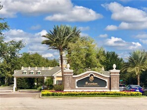 A golf resort entrance with a sign reading "Reunion Golf & Spa Resort," surrounded by palm trees and a flower bed. - Velleux Escape at Reunion Resort by Shine Villas (Kissimmee)