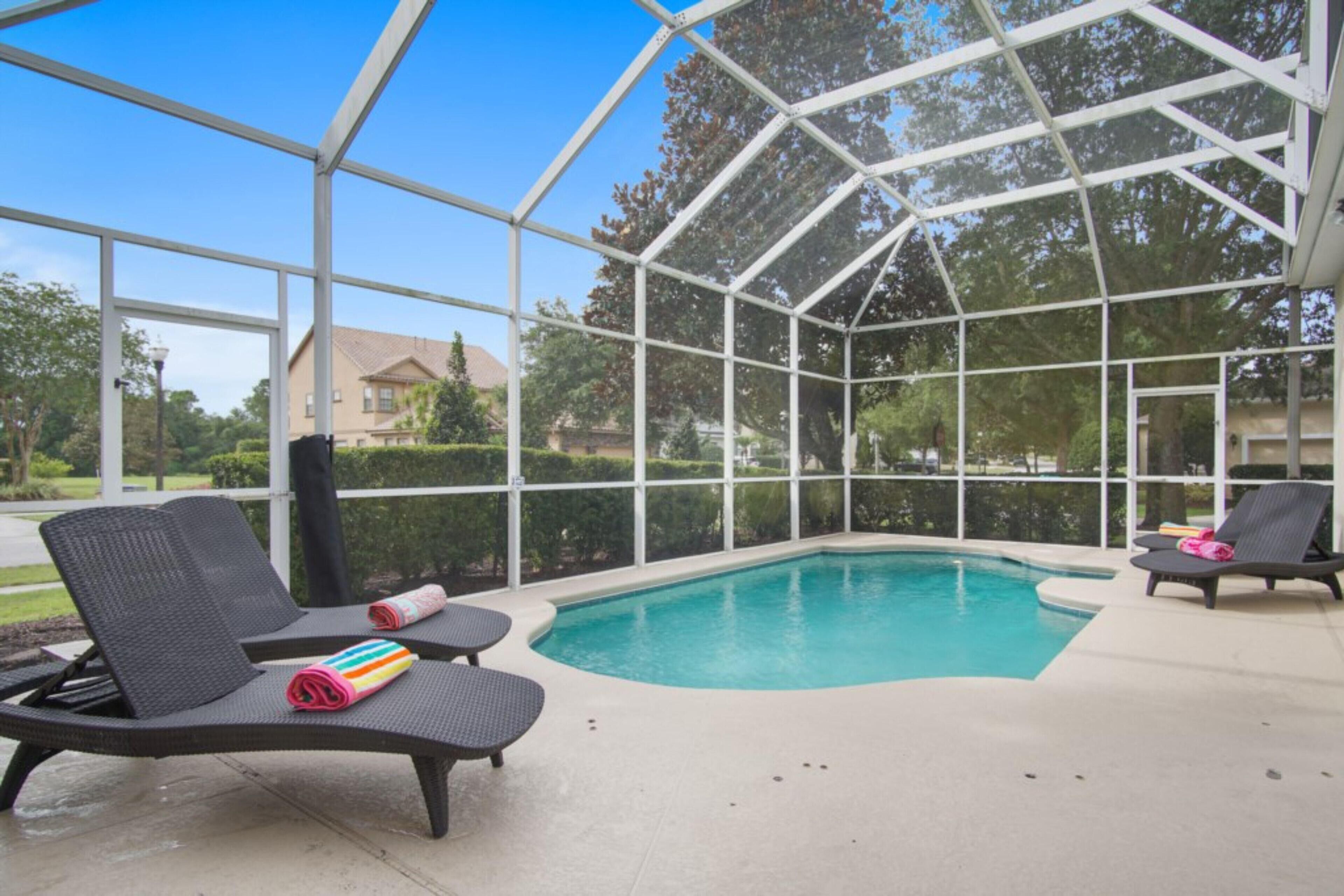A covered outdoor swimming pool with lounge chairs and a poolside table.