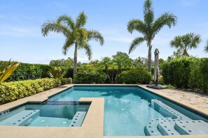 A rectangular swimming pool with a tiled deck, surrounded by palm trees and dense greenery. - Refurbished Lux 6 Bed Golf Views at Reunion Resort by Shine Villas (Kissimmee)